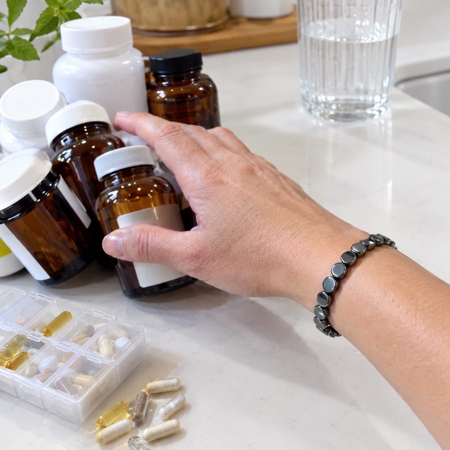 A hand wearing the HAIMA bracelet pushing a crowd of supplement bottles aside